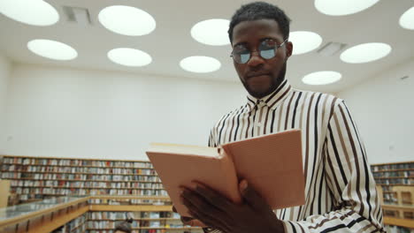 Hombre-Afro-Parado-En-La-Biblioteca-Y-Leyendo-Un-Libro